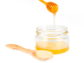 Jar of honey with wooden drizzler on white background