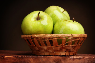 juicy green apples in basket on wooden table on brown background