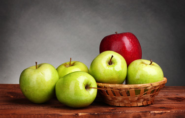 juicy sweet apples in basket on wooden table on gray background