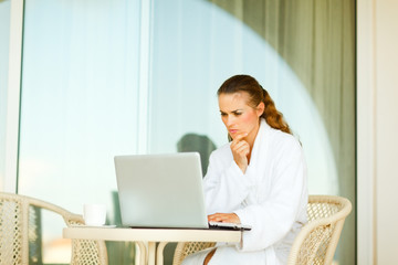 Serious attractive woman in bathrobe sitting at table on terrace