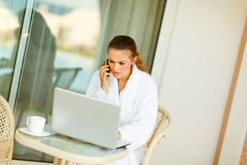 Concerned woman sitting at table on terrace speaking mobile