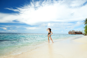 Fototapeta na wymiar Tranquil woman on the tropical beach with bungalows