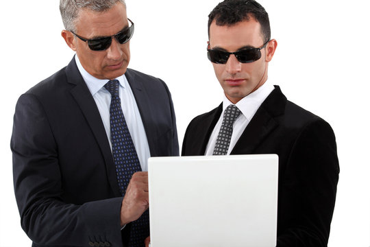 Serious men in smart suits with sunglasses holding a laptop