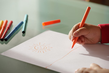 child drawing  a sun  with colorful markers close up hands