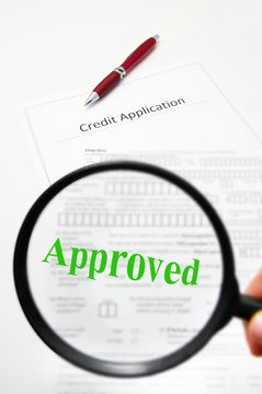 a credit application and magnifying glass with Approved text