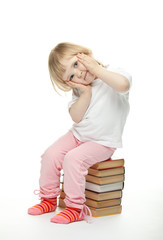 The baby girl is sitting on the books