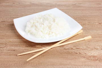 White bowl of cooked rice and chopsticks on wooden table