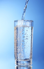 Pouring water on glass on blue background