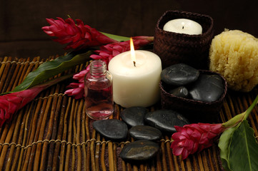 Fototapeta na wymiar burning candle and pebble with ginger flower on bamboo mat