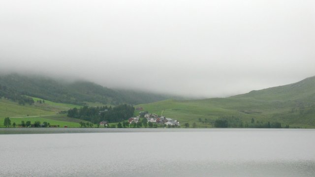 Calm lake in front of mountains covered with fog