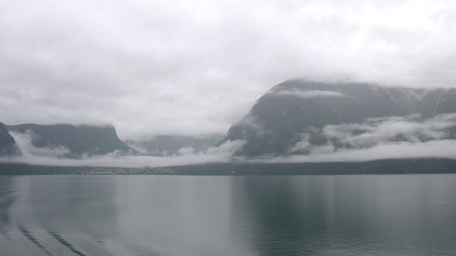 Calm lake in front of mountains covered with fog