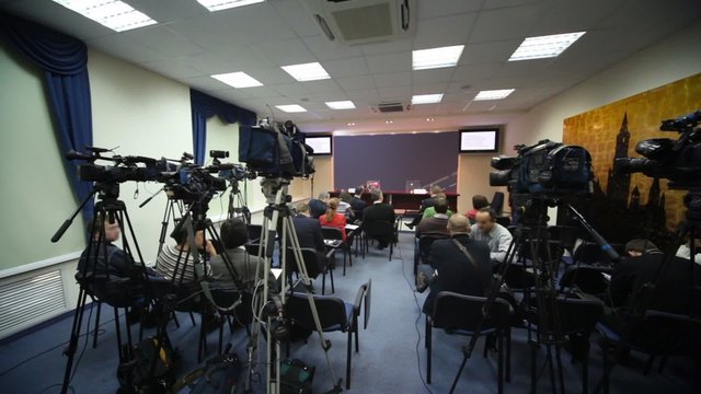 Journalists wait conference in press room, cameras stand around