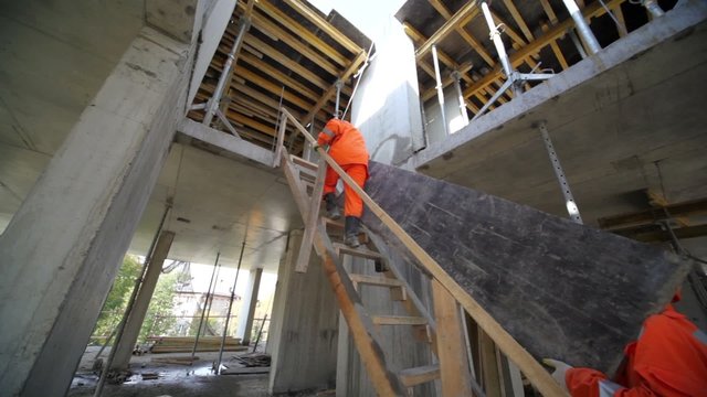 Two workers carry huge plate by wooden stairs to second storey