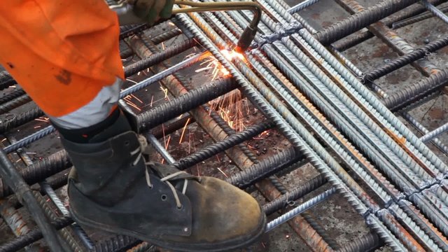 Worker legs in orange clothes weld metal grating
