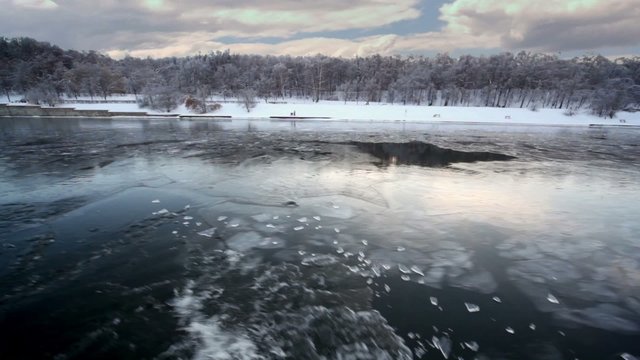 Sail through ice in river, which reflects forest on shore