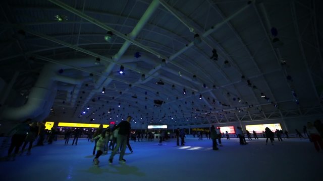 Many people skate on ice rink with colored illumination