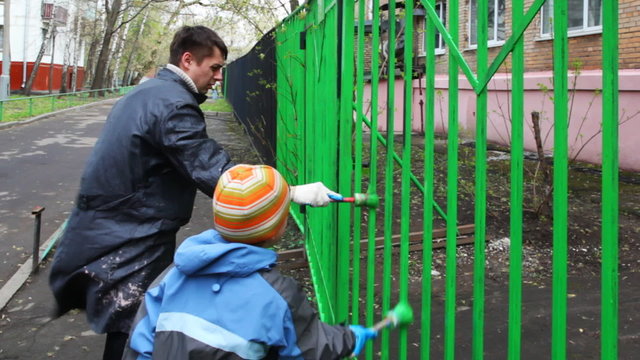 boy and father with paintbrush carefully dye fence by green