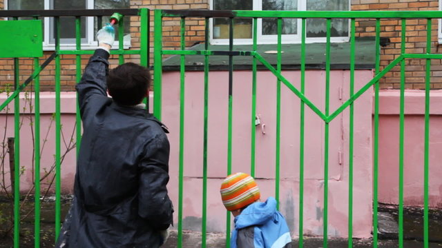 boy and father with paintbrush carefully dye fence by green