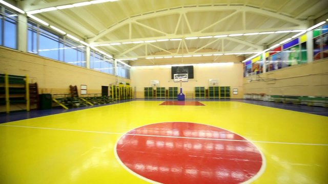 Inside lighted school gym hall with red yellow floor and basket