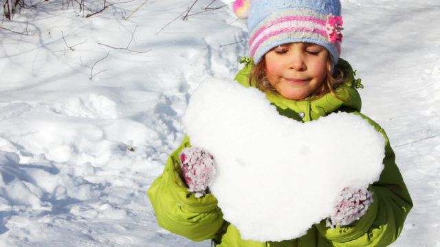 cute little girl hold heart made of snow and stand on trail