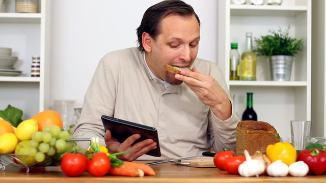 Man in kitchen with electronic tablet eat breakfast