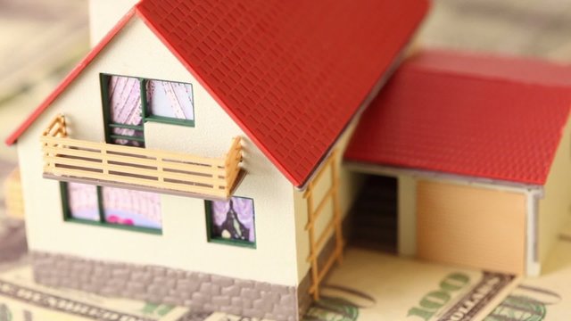 Toy house with red tiled roof on dollars bank notes