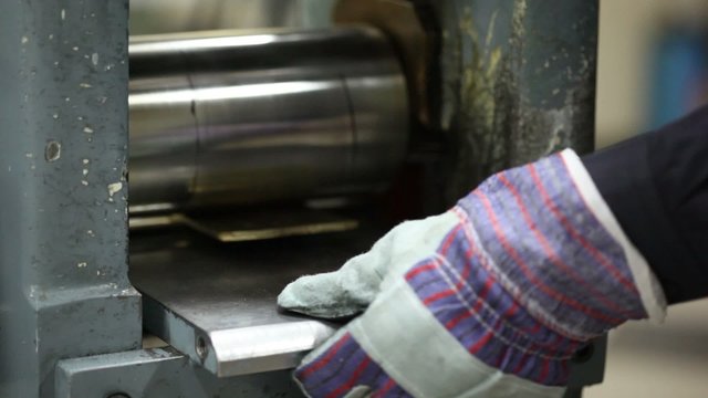 Man repeatedly inserts metal plate in rolling machine