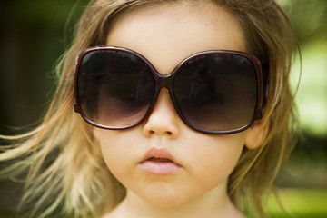 The little girl wears a large adult sunglasses