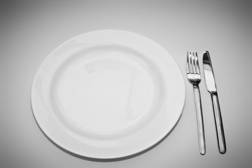 Weißer Teller mit Messer und Gabel vor vignettiertem Hintergrund