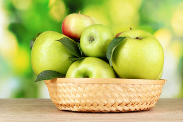 Fresh organic green apples in basket on wooden table outside