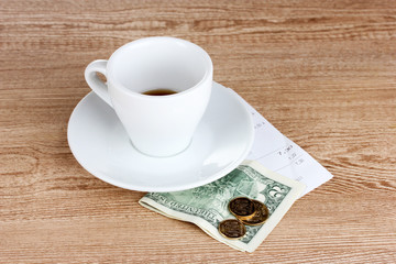 Empty cup of coffee with five dollars tip on wooden background