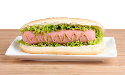 Delicious hot dog with mustard and lettuce on plate on wooden ba