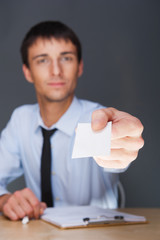 Business man handing a blank business card over grey background