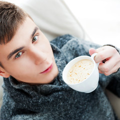 Obraz na płótnie Canvas Portrait of a young man drinking coffee while sitting on armchai