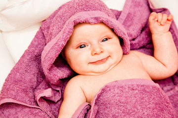 Obraz na płótnie Canvas Infant baby girl smiling laying in violet towel