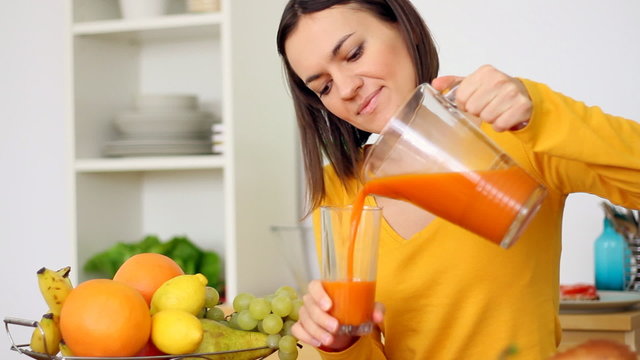 Happy woman pouring and drinking juice in the kitchen