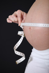 Pregnant woman holding a tape measure round her bump