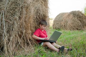 Naklejka na ściany i meble A boy with a laptop in the field