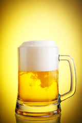 Glass of beer close-up with froth over yellow background