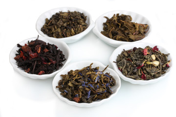 Green and black dry tea leaves in plates isolated on white