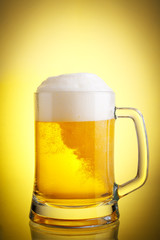 Glass of beer close-up with froth over yellow background
