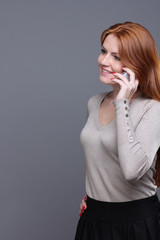 young woman talking on mobile phone against grey background