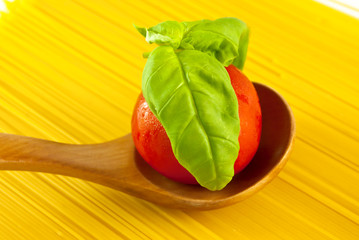 tomato and fresh basil on spoon in spaghetti background