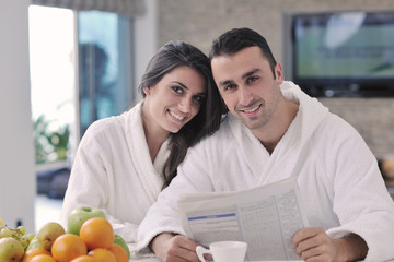 Happy couple reading the newspaper in the kitchen at breakfast