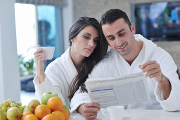 Happy couple reading the newspaper in the kitchen at breakfast