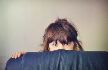 Fototapeta premium Little girl playing hide and seek behind the sofa
