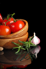 Tomatoes and garlic in wooden plate on black background.