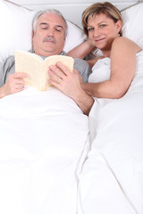 Obraz na płótnie Canvas Husband reading next to his wife in bed