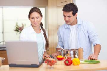 Obraz na płótnie Canvas Couple using a laptop to cook