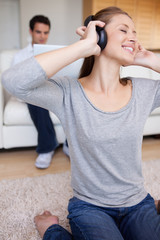 Naklejka premium Woman with earphones on the carpet and man behind her on the sof